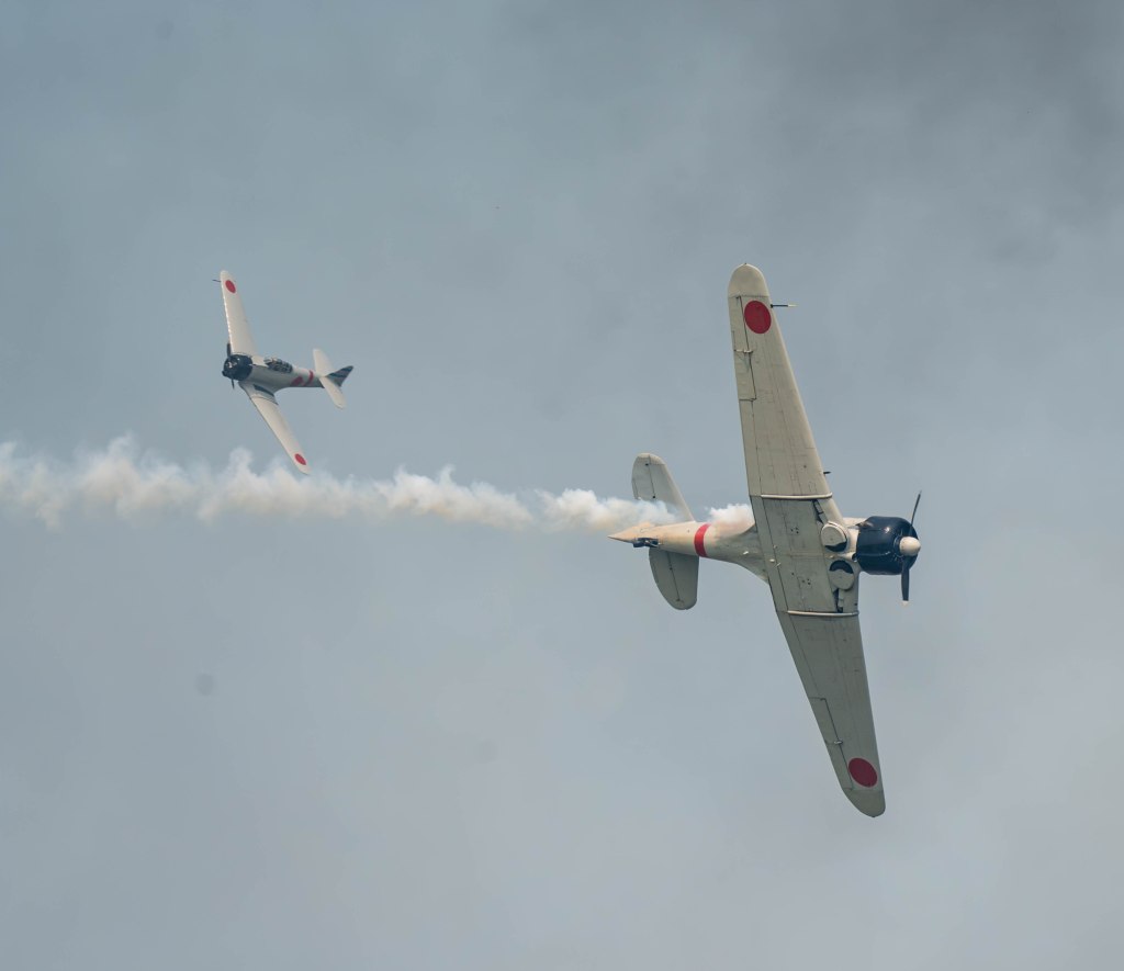 Two vintage aircraft performing aerial maneuvers in a cloudy sky, with smoke trailing from one plane.