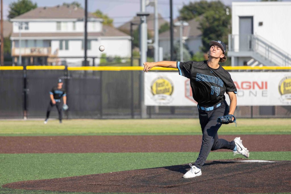 A young baseball pitcher wearing a black jersey with 'BENNINGTON' and the number 14 throws a baseball on a field. A teammate stands in the background.