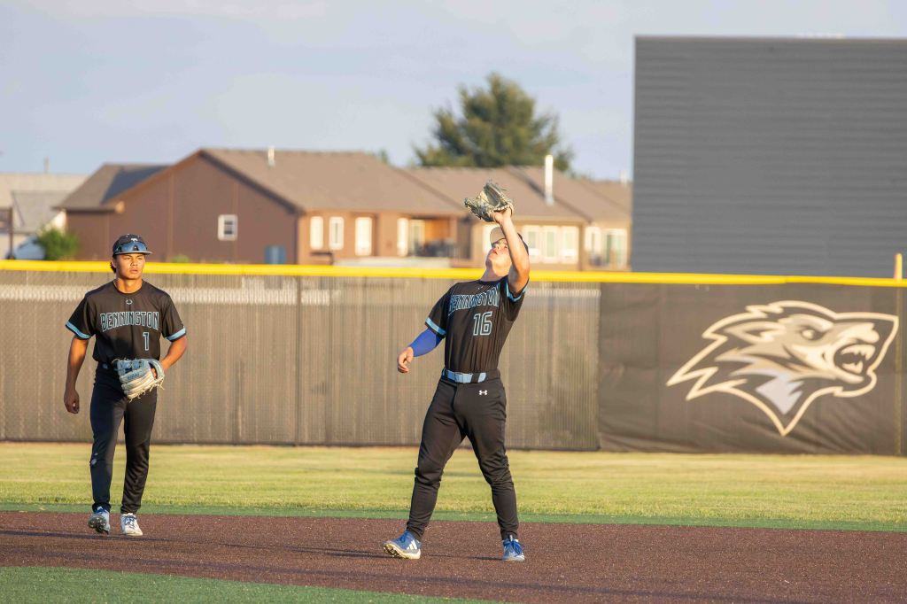 Two baseball players on the field. One is positioned in the outfield, catching a ball, while the other is nearby, ready for play.