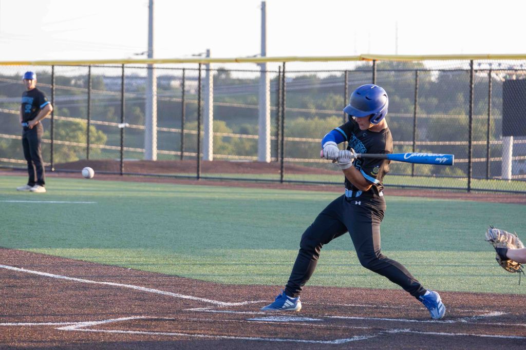 A young baseball player swinging a bat on a diamond while another player stands nearby, with a baseball in the foreground.