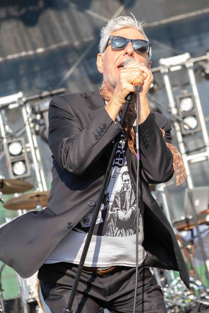 A male singer in a black suit and sunglasses passionately performing on stage with a microphone.