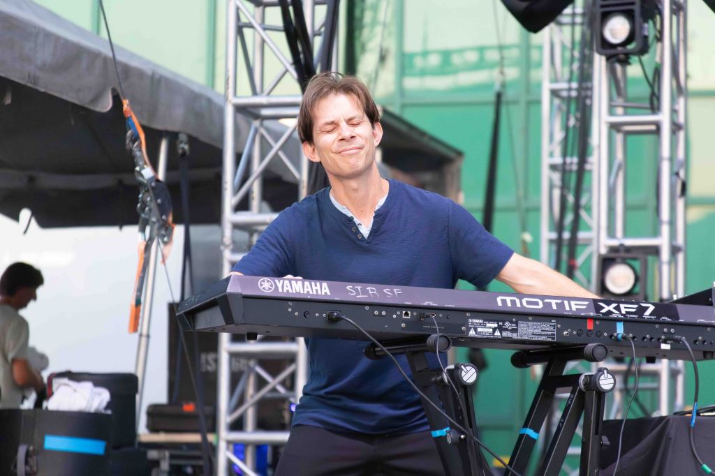 A musician playing a Yamaha keyboard on stage, expressing joy while performing, with stage lights and equipment in the background.