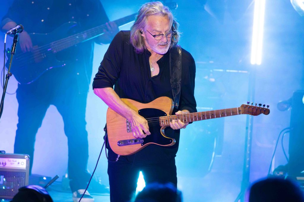 A musician playing an electric guitar on stage surrounded by colorful lighting and smoke.
