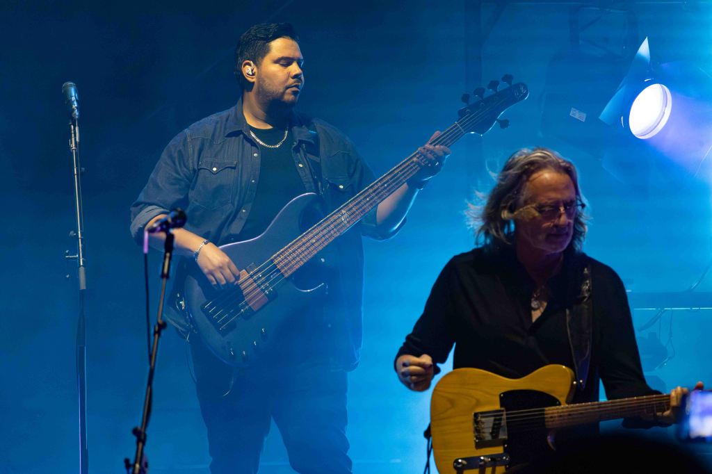 A musician playing a bass guitar on stage with blue lighting.