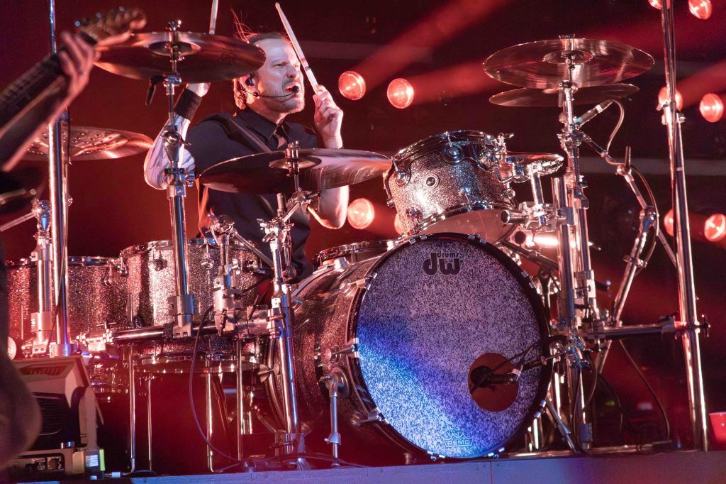 A drummer performing on stage with a sparkling drum set under bright stage lights.