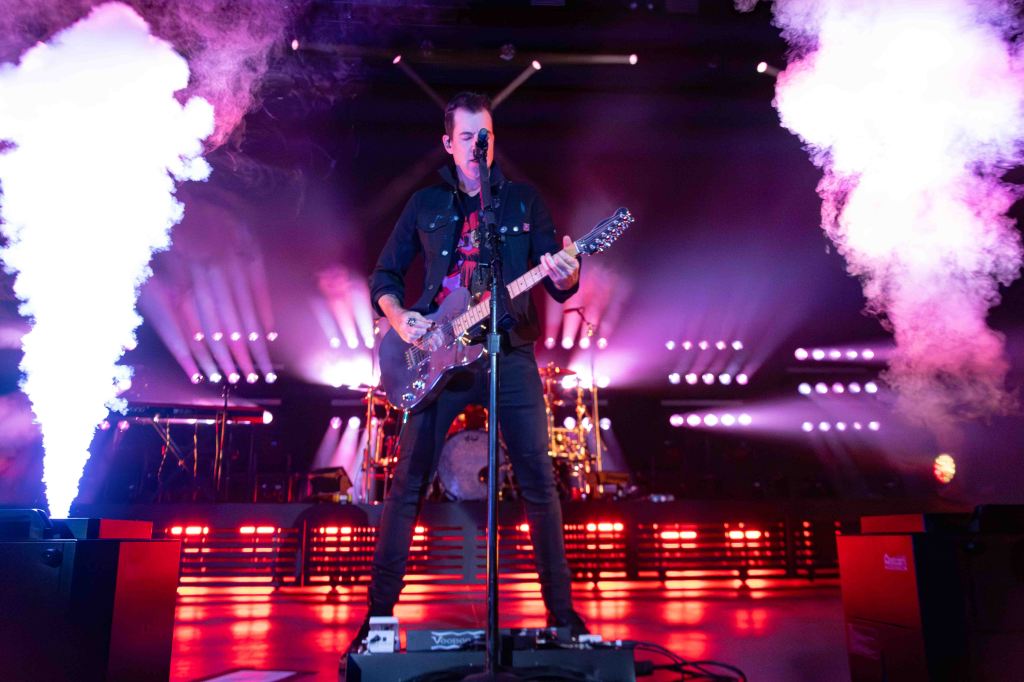 A musician performing on stage with a guitar, surrounded by smoke and dramatic lighting effects.