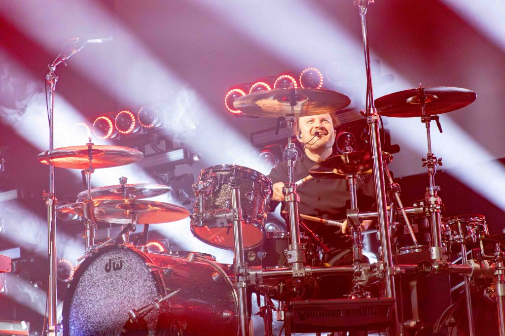 Drummer performing on stage with illuminated drum set and vibrant stage lights.