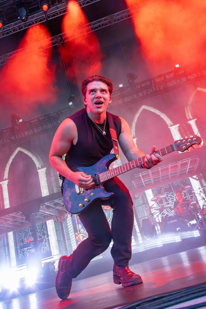 A musician performing on stage, passionately playing a blue electric guitar with dramatic stage lighting in the background.