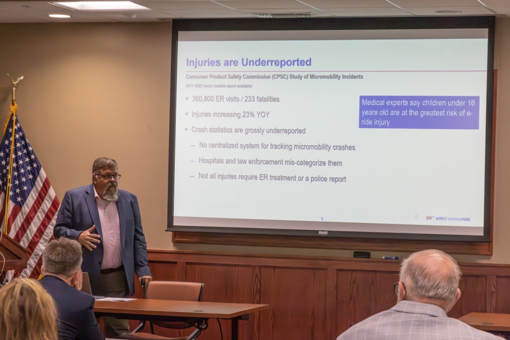 A speaker presenting information about underreported injuries related to micromobility incidents, with key statistics displayed on a screen behind them.