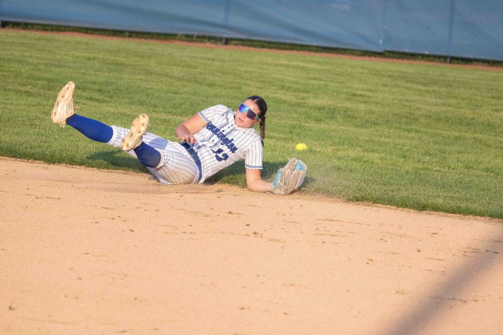 A softball player in a striped uniform is sliding on the ground while attempting to catch a ball on the field.