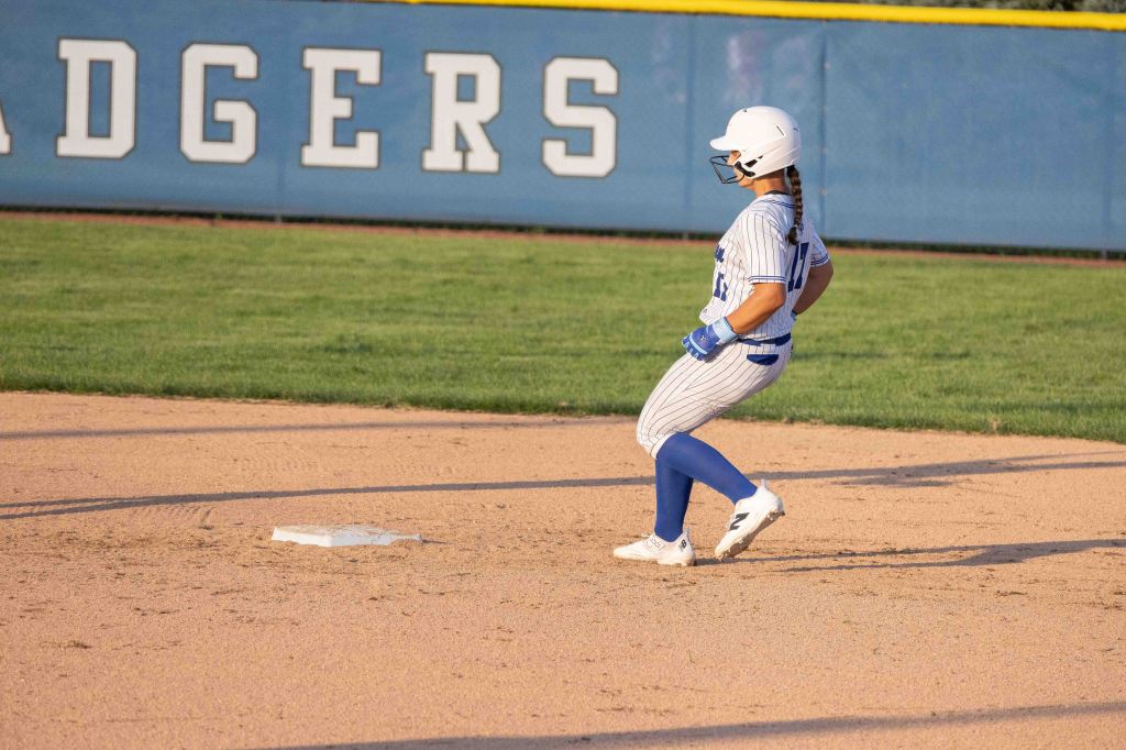 A female softball player sliding into a base during a game, wearing a striped uniform with blue accents.