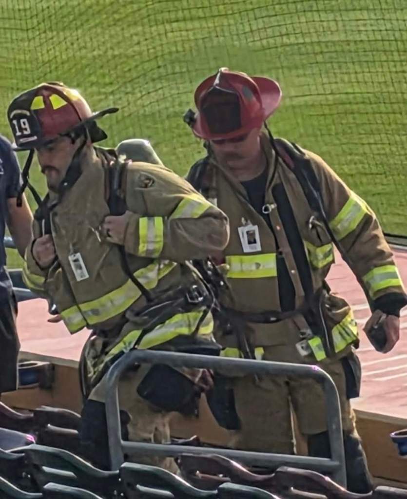 Two firefighters in full gear walking in a stadium, preparing their equipment.