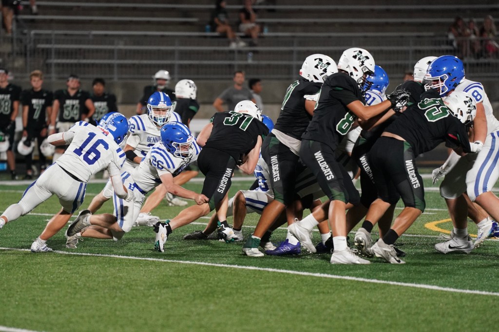 A high school football game in progress with players in blue and black uniforms competing on the field, showcasing a play where a blue team player is attempting to tackle a black team player.