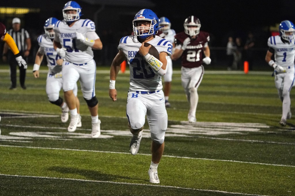 A football player in a blue and white uniform running with the ball on the field, surrounded by other players in action.