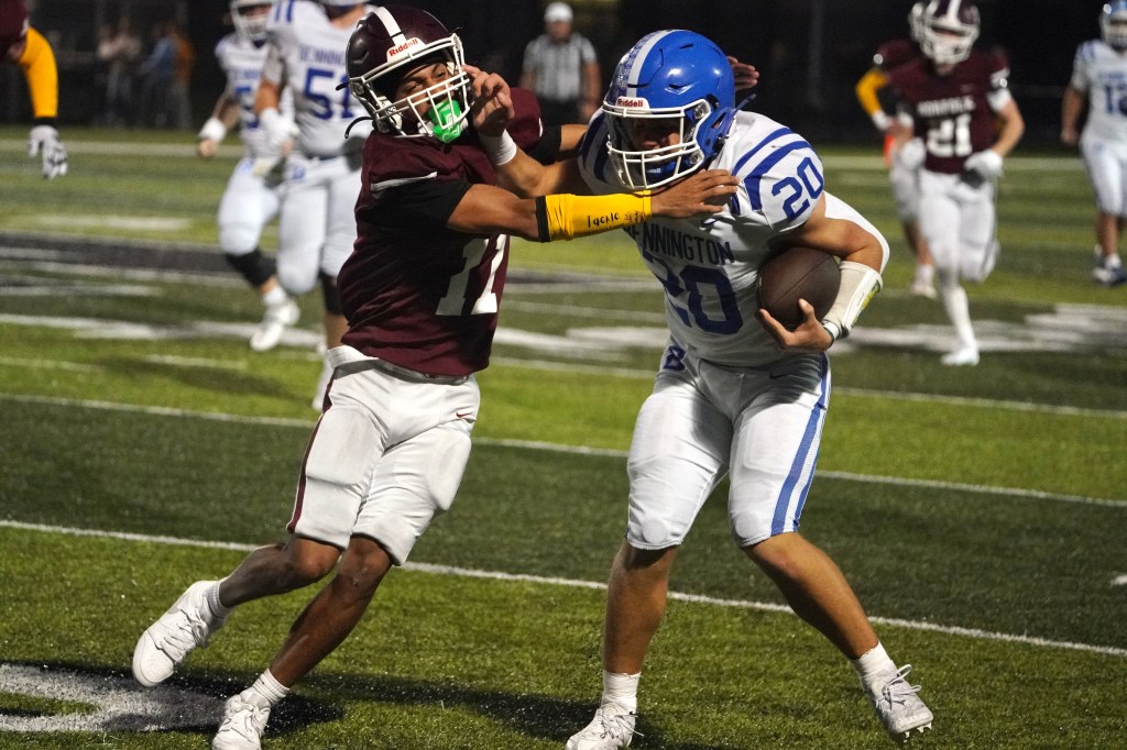A football player in a blue jersey is being tackled by an opponent in a maroon jersey on a field.
