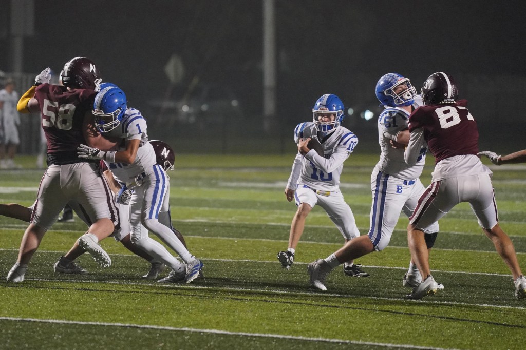 A tense moment in a nighttime high school football game, featuring players in blue and maroon uniforms. A player in blue (#1) attempts to tackle an opponent wearing maroon (#58) as teammates look on, revealing the intensity of competition on the field.