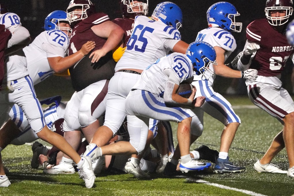A football player in a blue uniform, number 25, is attempting to navigate through a pile of players during a game. Several players from both teams are engaged in the tackle.