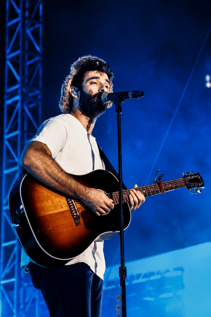 A singer performing on stage with an acoustic guitar under blue lighting.