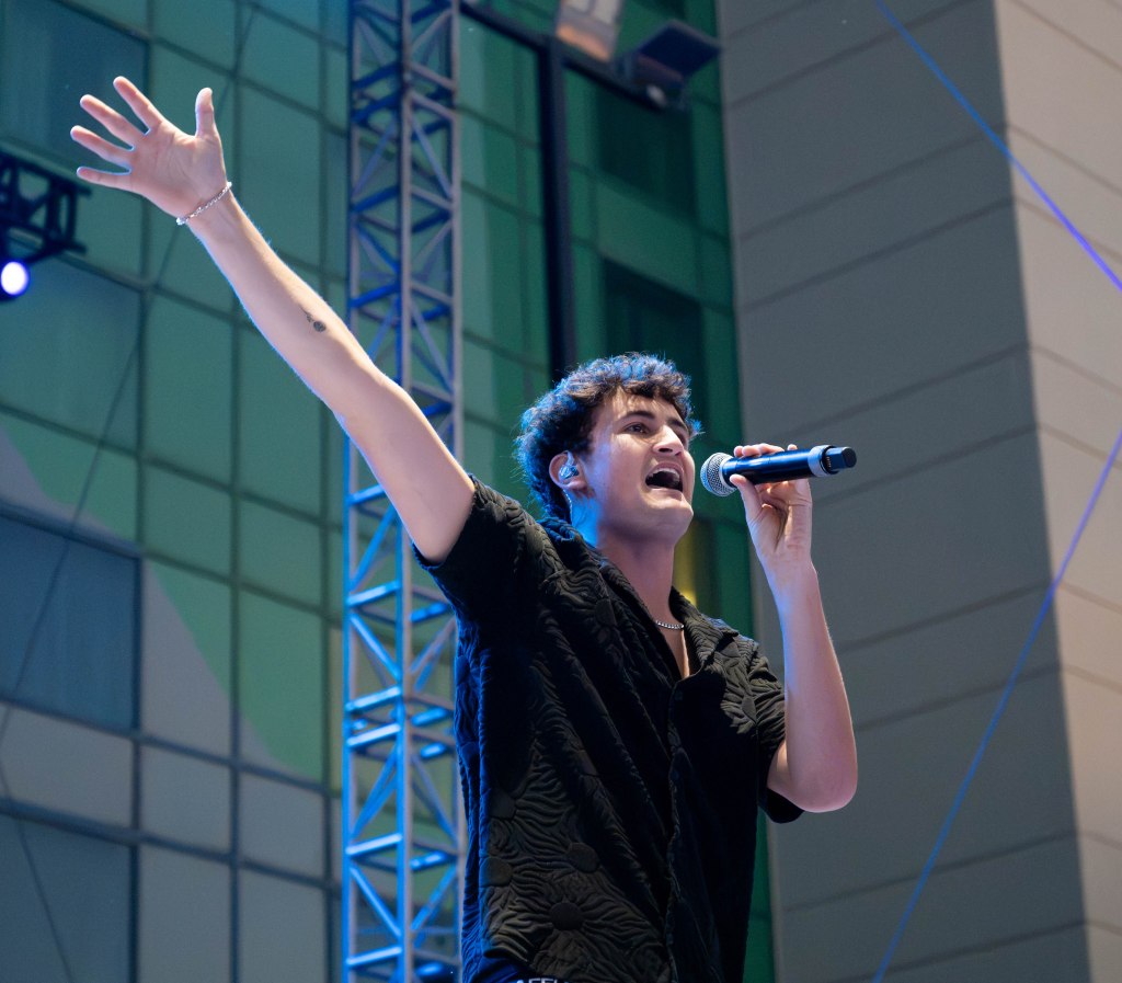 A singer performing on stage with one arm raised, holding a microphone, and expressing energy and enthusiasm.