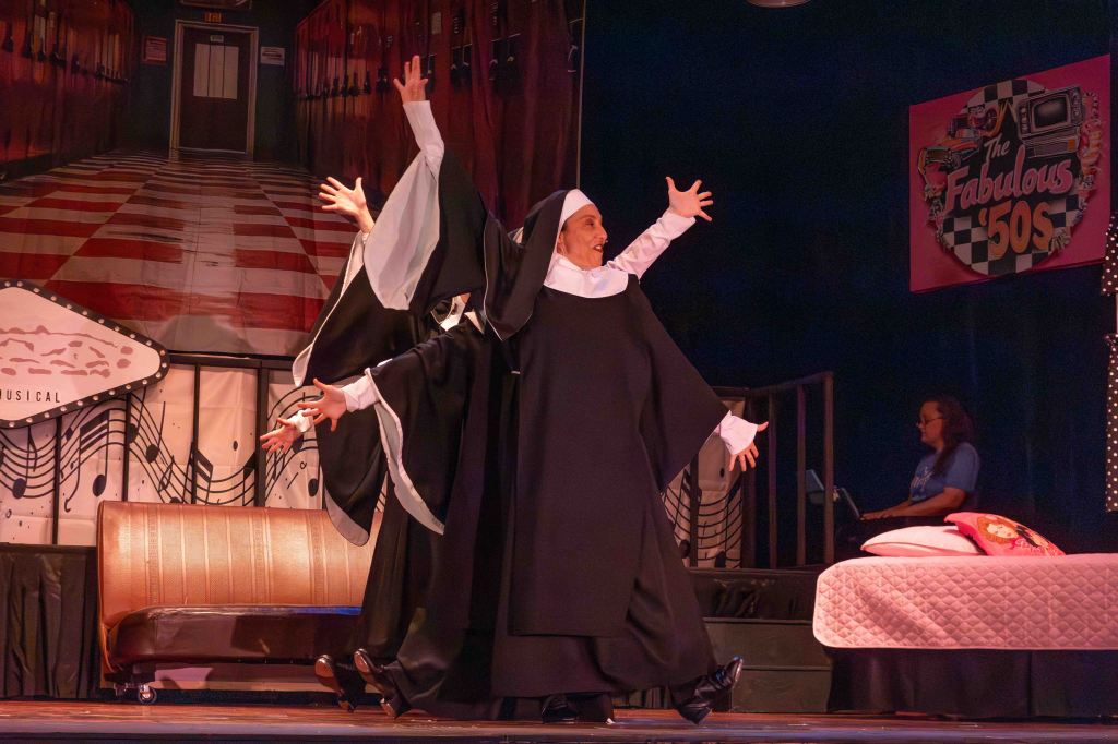 Two nuns performing on stage with enthusiastic poses, set against a colorful backdrop featuring a retro theme.