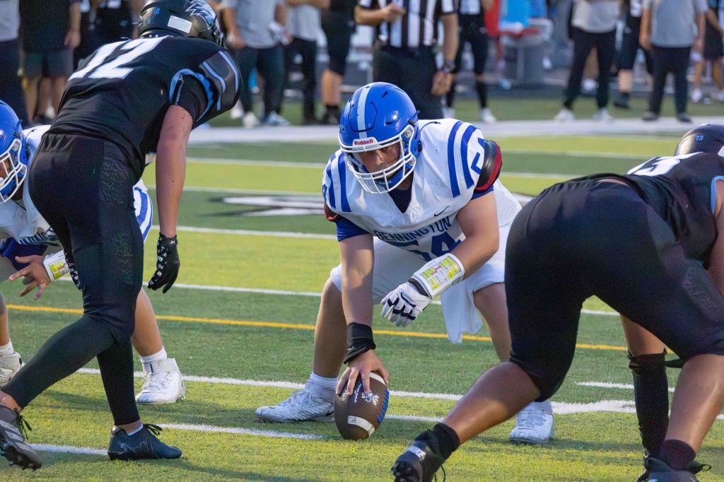 A youth football game in progress, featuring a center preparing to snap the ball while opposing players crouch on the line of scrimmage.