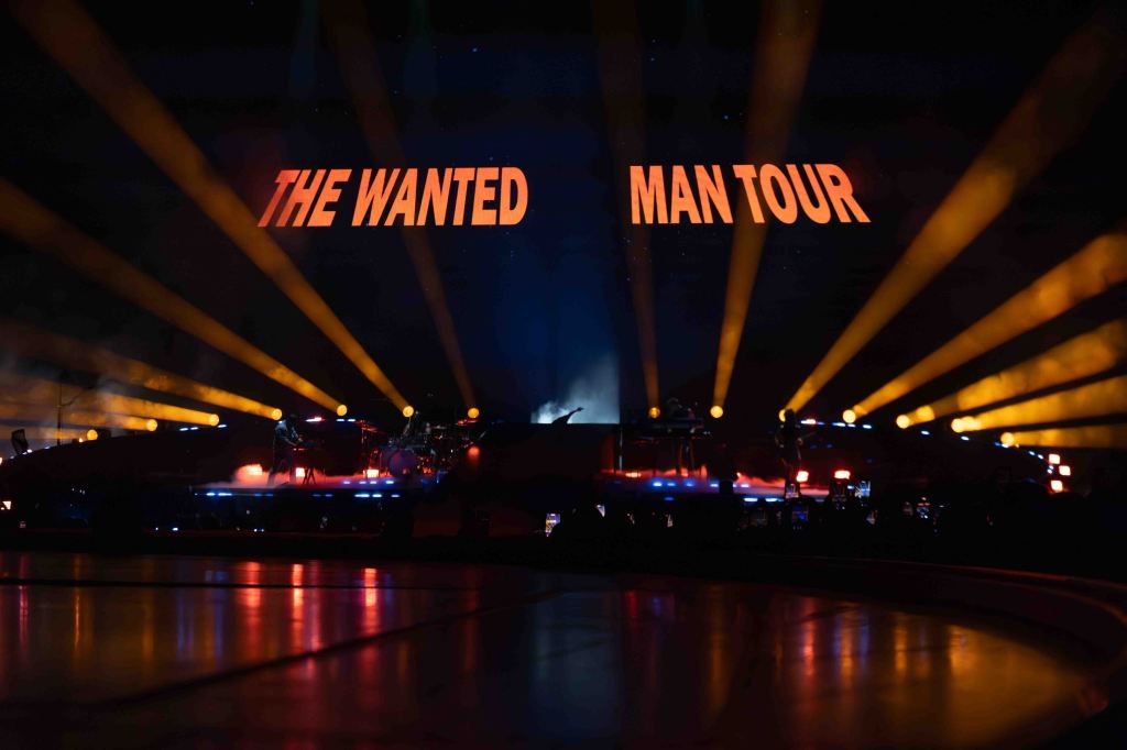 Stage lights and backdrop displaying 'THE WANTED MAN TOUR' during a concert performance.