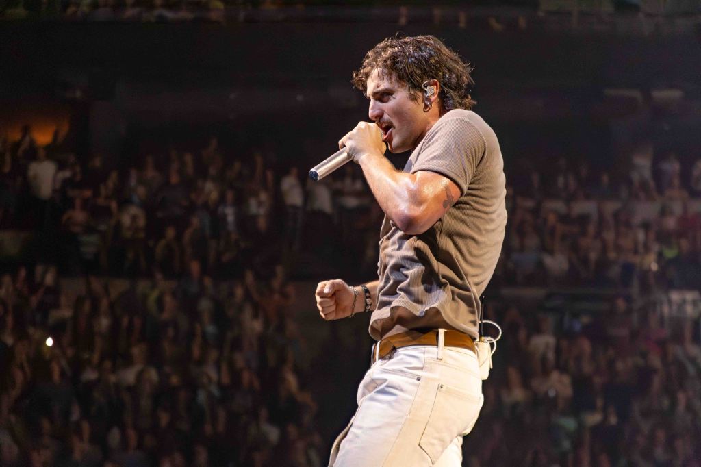 A male singer performing on stage, holding a microphone and engaging with the audience in a packed concert venue.