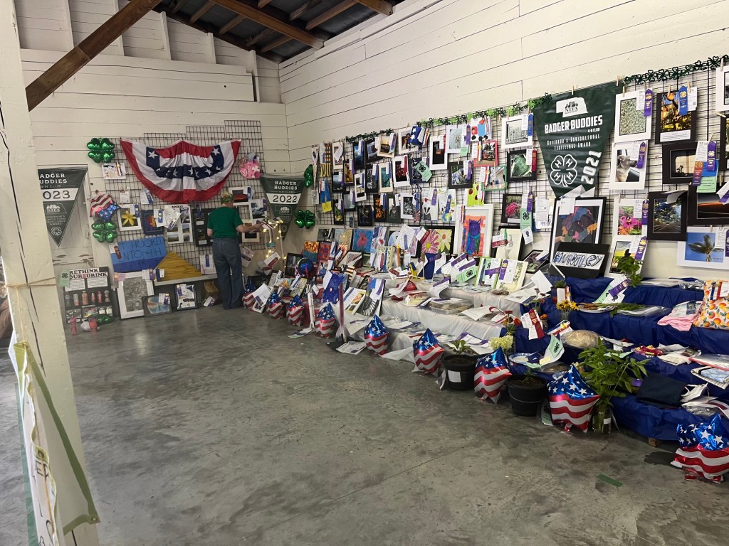 A decorated exhibition space featuring various artworks, photographs, and display items related to a community event, with banners and decorations in red, white, and blue.