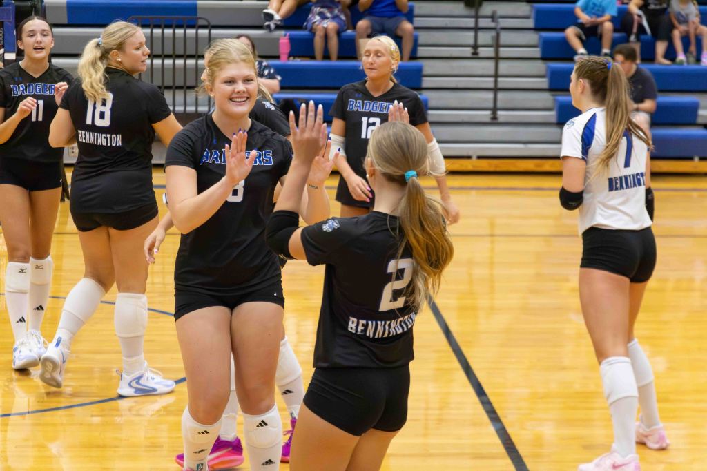 A volleyball team celebrating together on the court, high-fiving each other in a supportive gesture, with players wearing black and white jerseys.