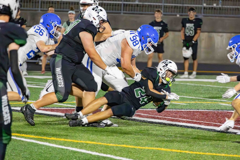 A football player wearing a black jersey with the number 24 is being tackled on the field by opponents in blue jerseys during a game.