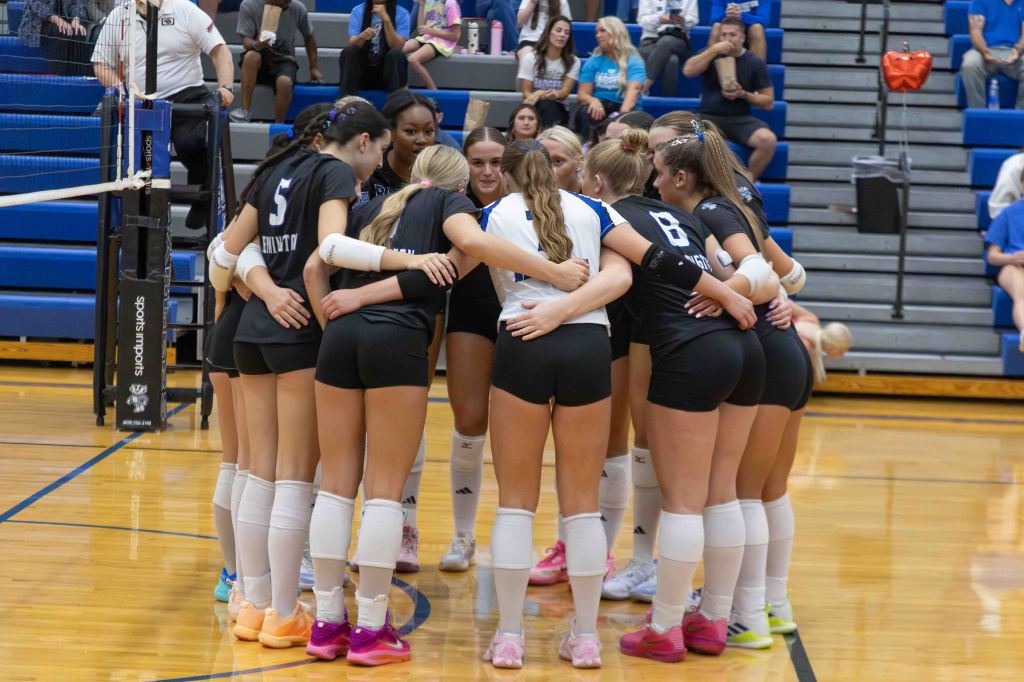A group of young female volleyball players huddled together on the court, focusing and motivating each other before a match.