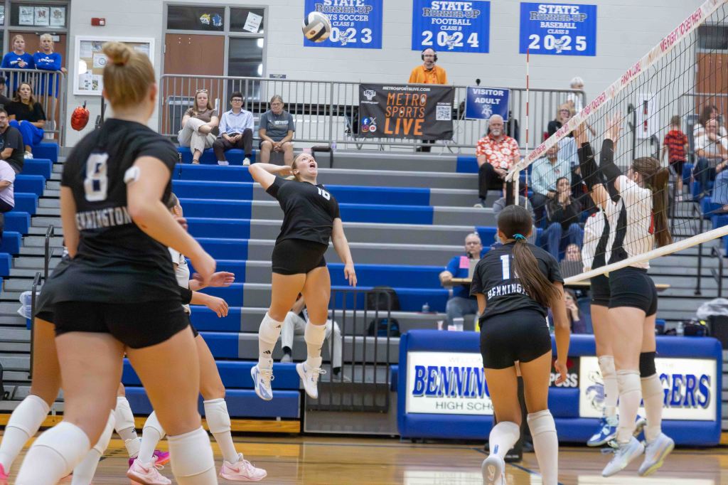 A volleyball player in mid-air preparing to hit the ball during a game, with teammates and spectators visible in the background.
