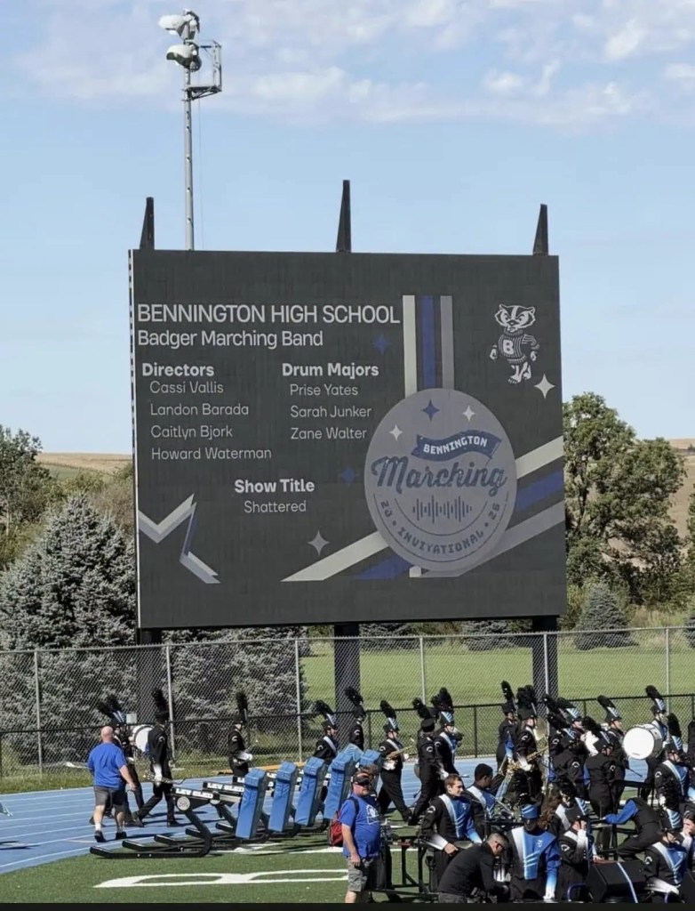A digital marquee displaying the Bennington High School Badger Marching Band details, including directors, drum majors, and the show title 'Shattered'.