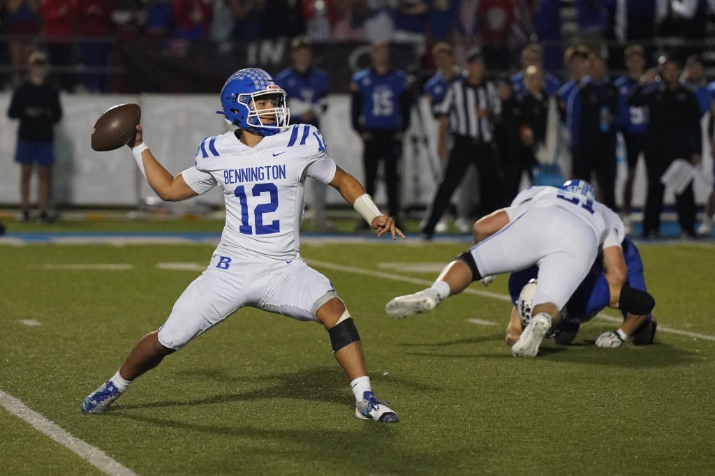 A football player in a white uniform with 'Bennington' written on it, wearing a blue helmet, is in the process of throwing a football while another player is on the ground behind him.