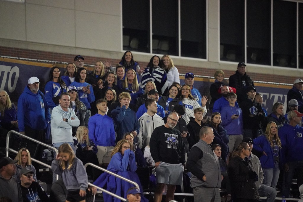 A crowd of fans wearing blue attire gathered in a stadium, some waving and smiling, showing enthusiasm during a sporting event.
