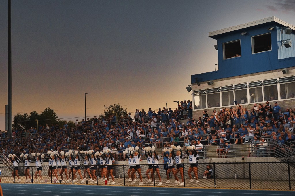 Cheerleaders performing in front of a large crowd at a football stadium during sunset.