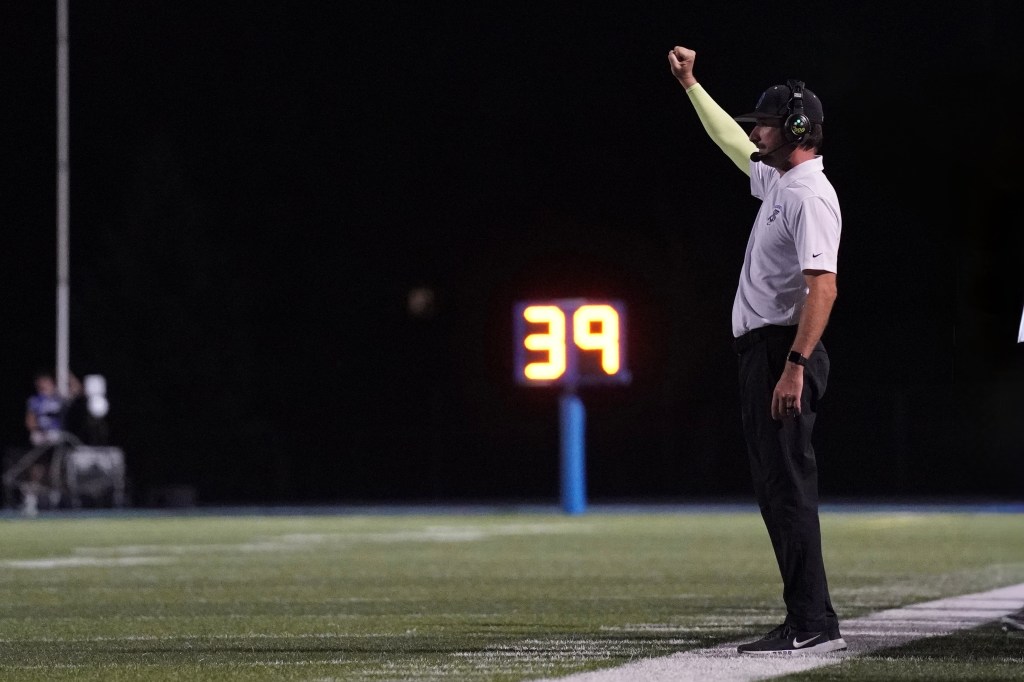 Football coach signaling with a raised fist on the sidelines during a night game, with a game clock displaying 39 seconds.