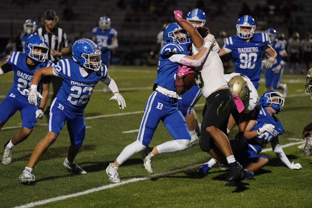 A dynamic football scene featuring players in blue jerseys from the Badgers team tackling an opponent in a white jersey during a night game.