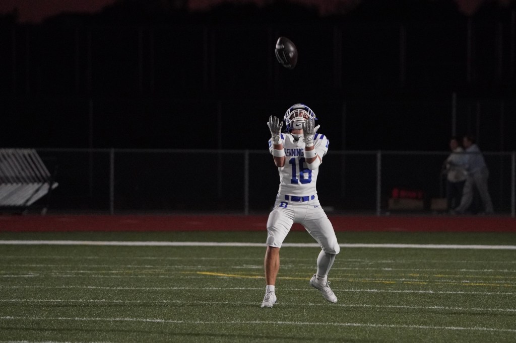 A football player in a white uniform preparing to catch a football under stadium lights at night.