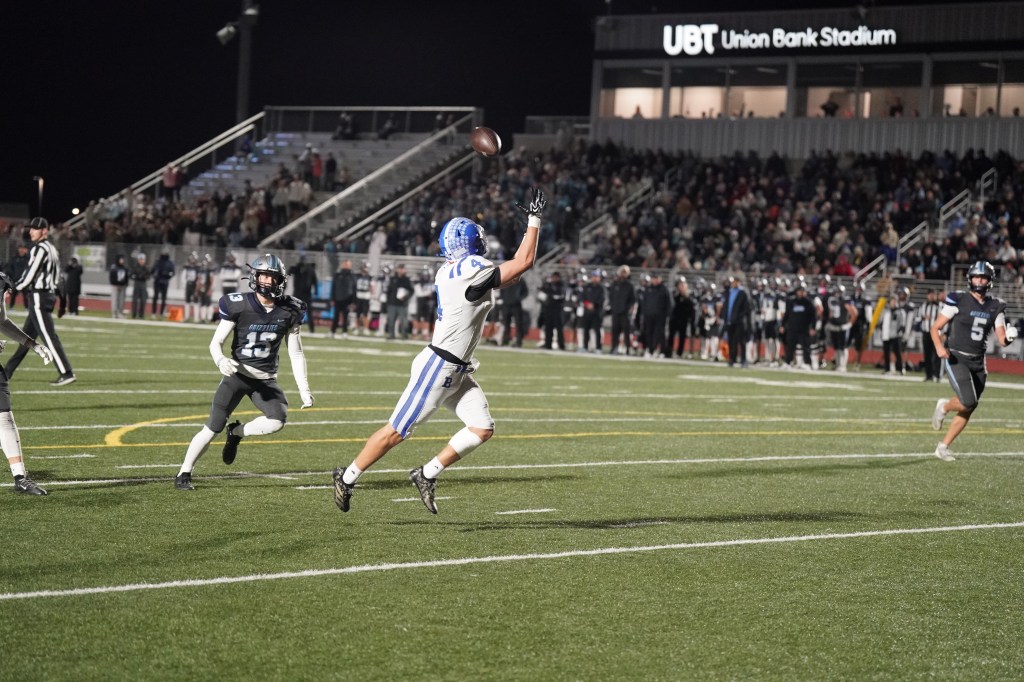 A football player in a white and blue uniform leaps to catch a flying football during a night game at Union Bank Stadium, with the opposing team and spectators visible in the background.