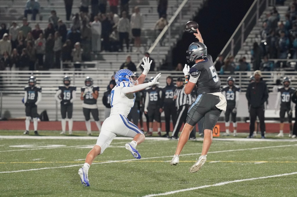 A football player in dark uniforms throws a pass while being challenged by a defender in white uniforms during a night game.