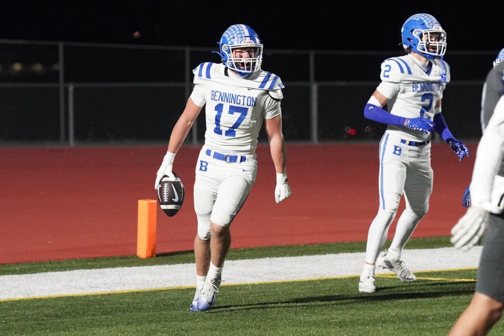 A football player wearing a white and blue uniform with 'Bennington' on the front celebrates while holding a football, with a teammate in the background.