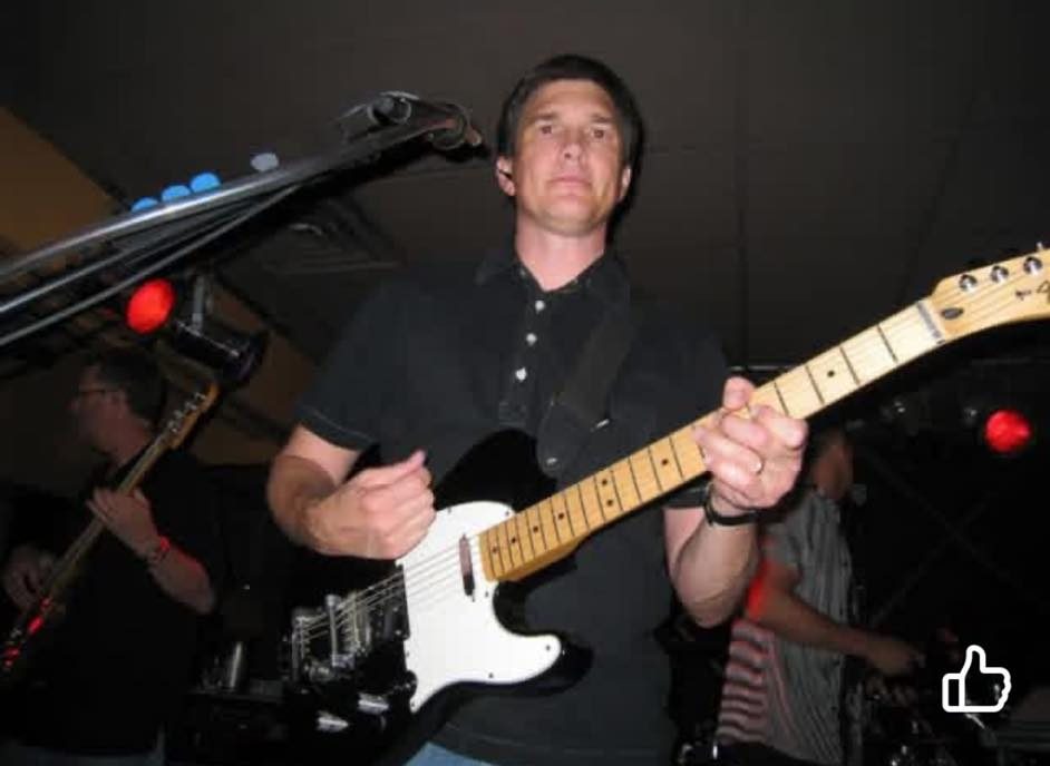 A musician playing an electric guitar on stage with colorful lights in the background.
