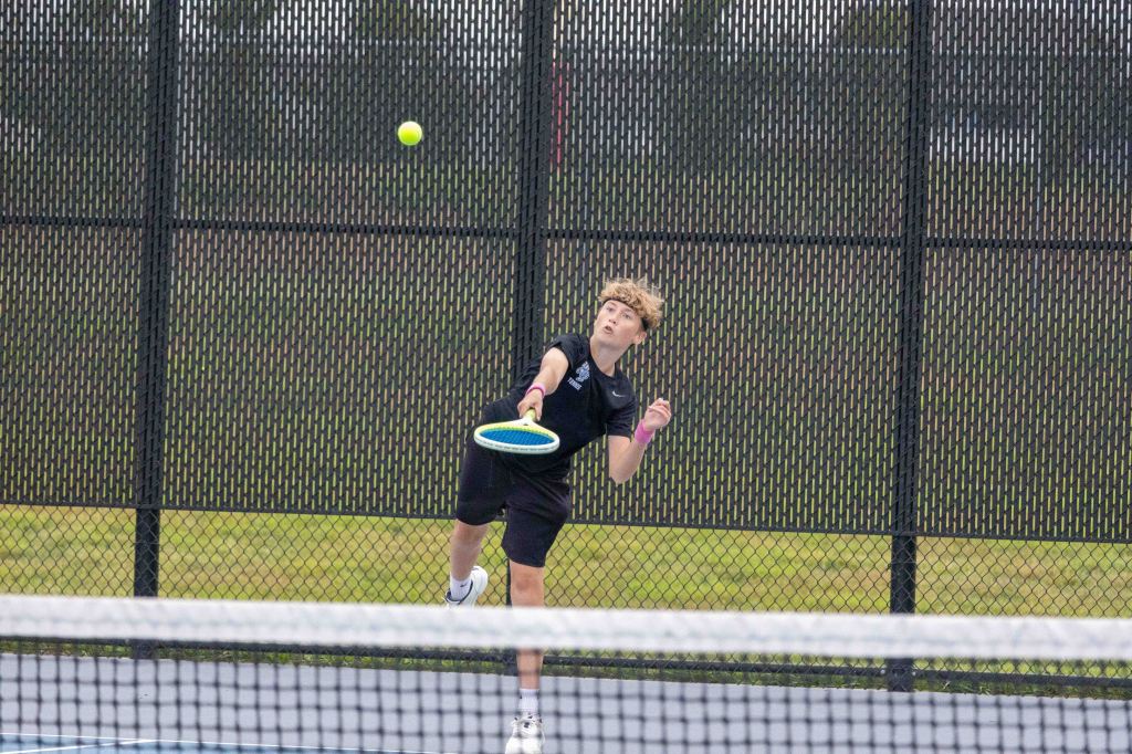 A young male tennis player serving the ball on a court, with a focus on his motion and concentration.