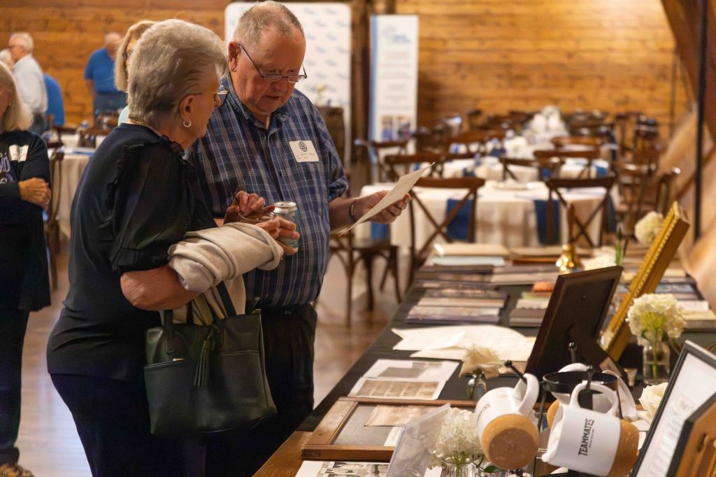 Two people examining materials at an event, with tables set up in a decorated venue.