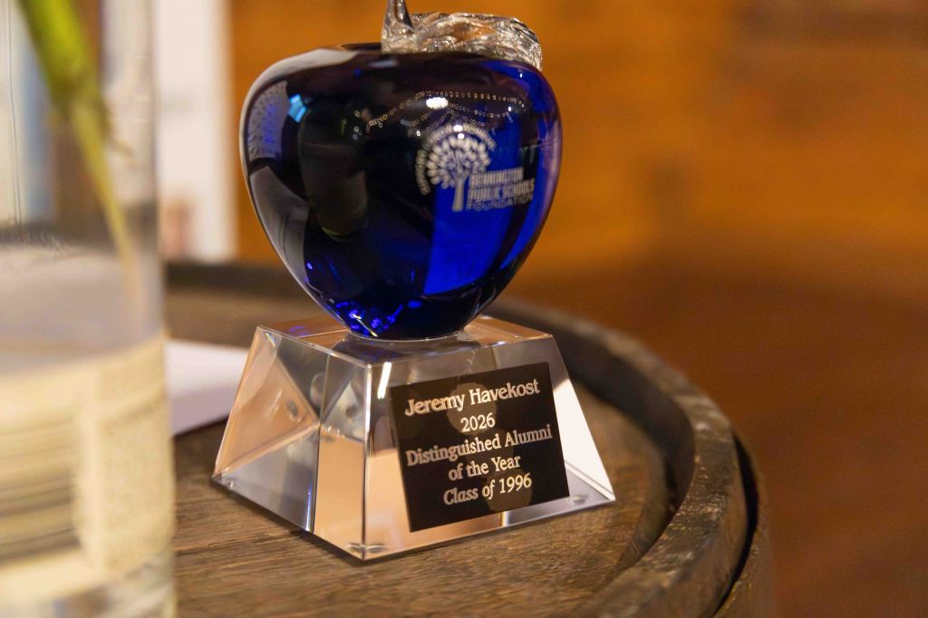 A blue glass apple award on a clear base displaying an engraving that reads 'Jeremy Havekost 2026 Distinguished Alumni of the Year Class of 1996'.