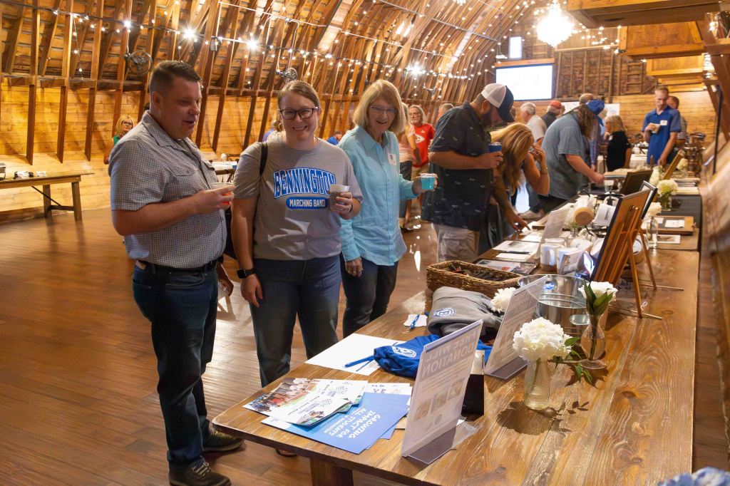 People interacting at a community event inside a rustic barn, with tables displaying promotional materials and refreshments.