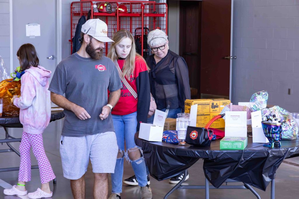 Three people inspecting tables filled with various items at an event.