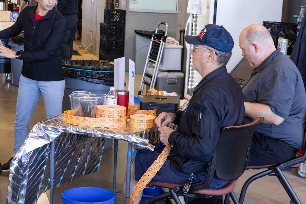 Two individuals seated at a table with various game tickets and cups; one person is holding a roll of tickets while the other looks on.