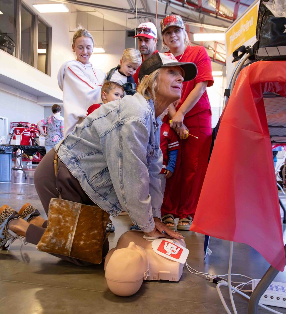 A group of people observing a woman performing CPR on a training dummy at a community event, demonstrating emergency response techniques.